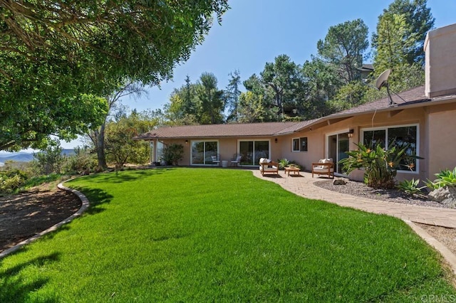 back of house with stucco siding, a patio, and a yard