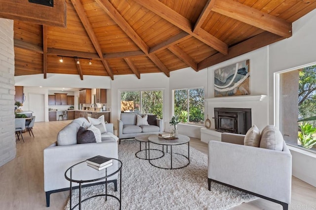 living room featuring high vaulted ceiling, wood ceiling, a fireplace with raised hearth, and light wood finished floors