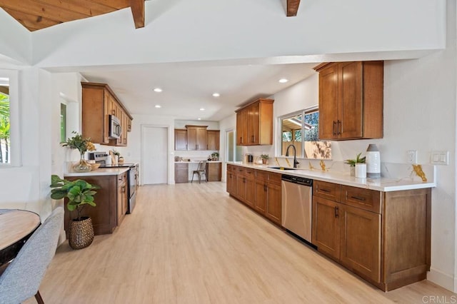 kitchen featuring light wood-style flooring, a sink, stainless steel appliances, brown cabinetry, and light countertops