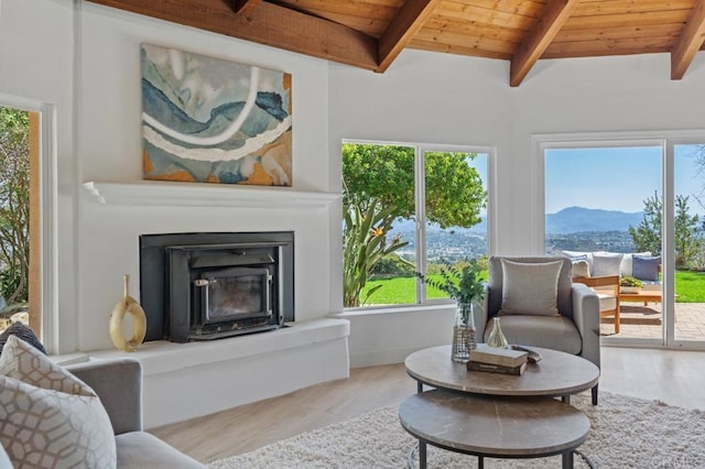 living area with wood finished floors, a glass covered fireplace, a mountain view, wood ceiling, and vaulted ceiling with beams