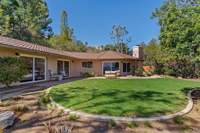 back of house with stucco siding, a lawn, a chimney, and a patio area