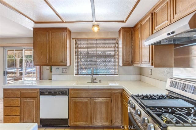 kitchen with white dishwasher, under cabinet range hood, a sink, stainless steel gas stove, and brown cabinetry