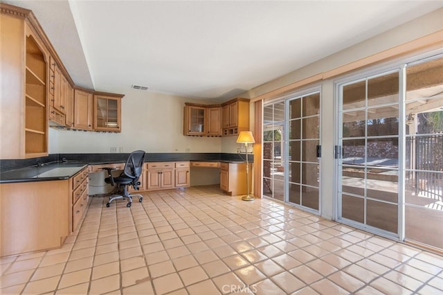 kitchen with dishwashing machine, open shelves, built in desk, dark countertops, and glass insert cabinets