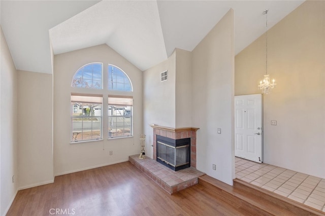 unfurnished living room with a glass covered fireplace, visible vents, a notable chandelier, and wood finished floors