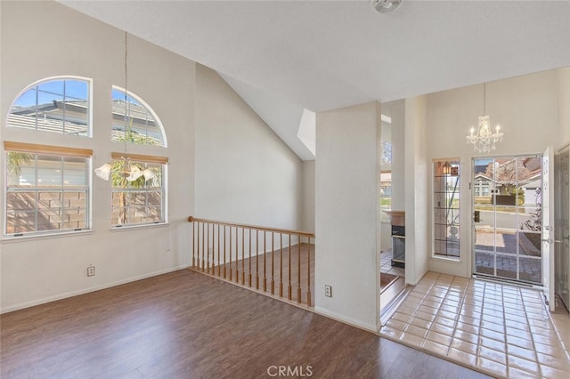 unfurnished room with wood finished floors, a towering ceiling, baseboards, and an inviting chandelier