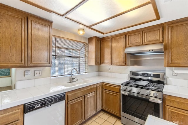 kitchen featuring brown cabinets, a sink, dishwasher, under cabinet range hood, and stainless steel gas range oven