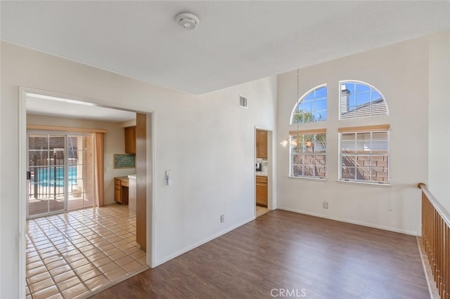 spare room featuring visible vents, a towering ceiling, baseboards, and wood finished floors