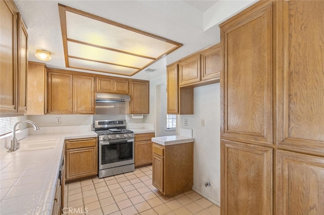 kitchen with stainless steel gas range oven, range hood, tile counters, and visible vents