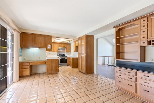 kitchen featuring stainless steel range, built in study area, light countertops, under cabinet range hood, and a sink