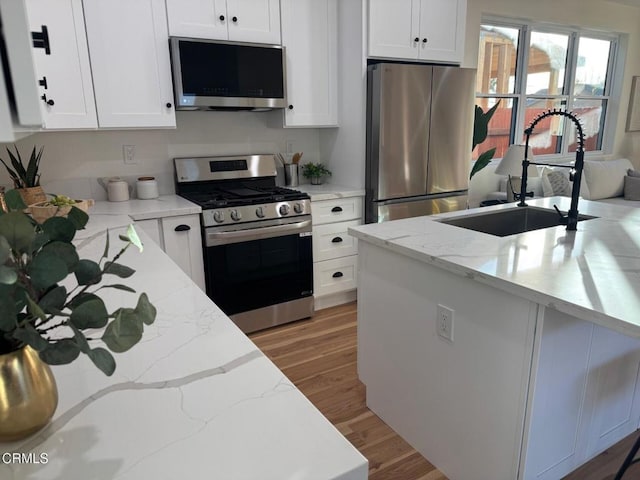 kitchen with stainless steel appliances, white cabinetry, a sink, and light wood finished floors
