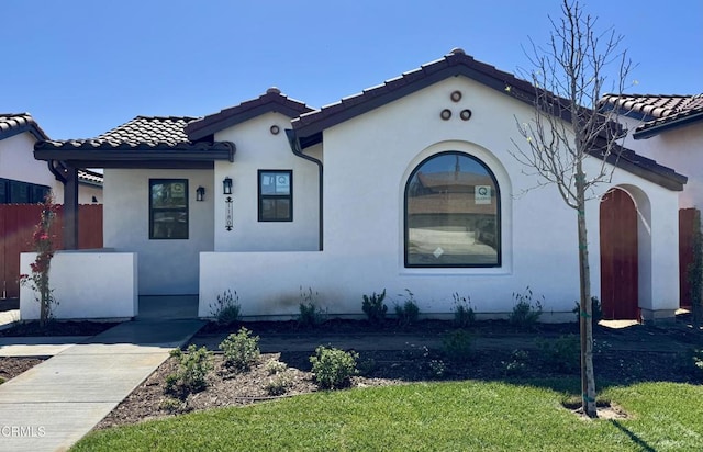mediterranean / spanish-style house featuring a front yard, fence, a tiled roof, and stucco siding