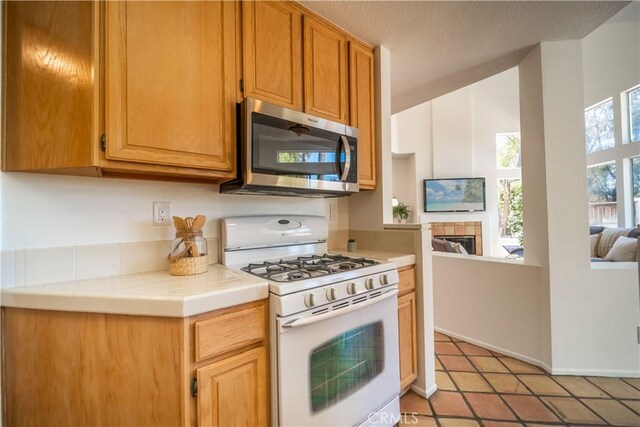 kitchen with white gas stove, stainless steel microwave, a textured ceiling, a fireplace, and tile counters