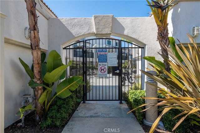 doorway to property featuring stucco siding, fence, and a gate