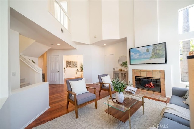 living area featuring stairs, recessed lighting, a tile fireplace, a towering ceiling, and wood finished floors