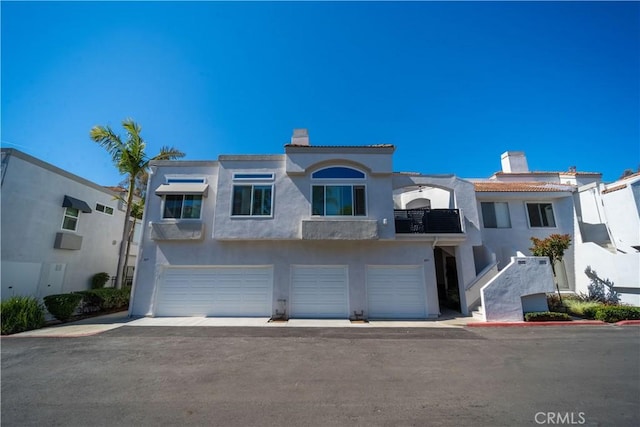 view of front of house featuring a balcony, a garage, a chimney, and stucco siding