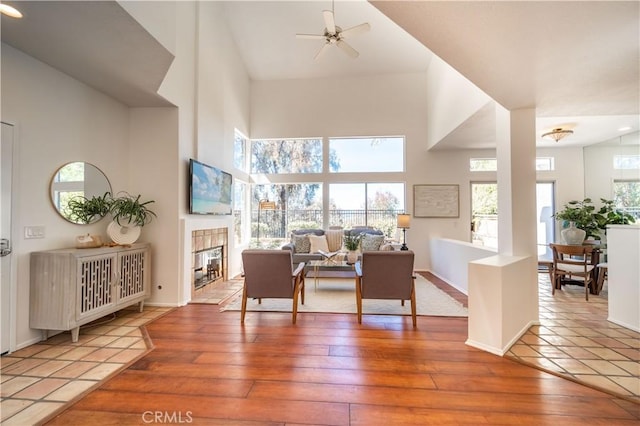 interior space featuring a ceiling fan, wood-type flooring, a fireplace, baseboards, and a towering ceiling