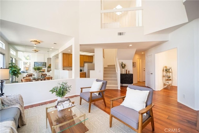 living area featuring light wood-type flooring, visible vents, a high ceiling, baseboards, and stairs