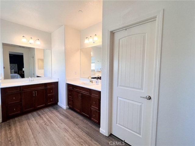 ensuite bathroom with a sink, wood finished floors, two vanities, and connected bathroom