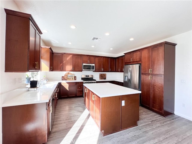 kitchen featuring light countertops, appliances with stainless steel finishes, light wood-type flooring, and a center island