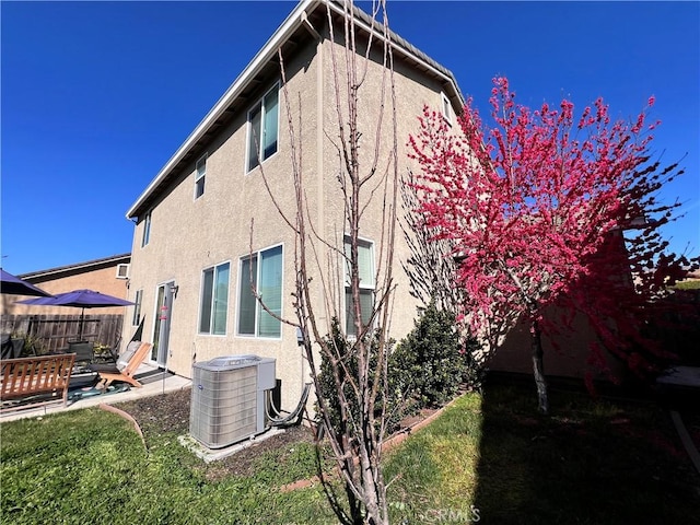 rear view of property with a patio area, fence, central AC unit, and stucco siding