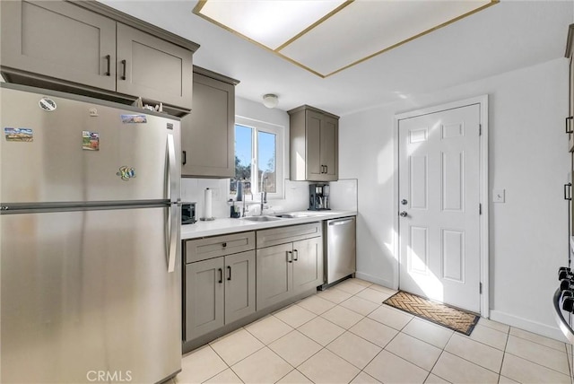 kitchen with gray cabinets, light countertops, appliances with stainless steel finishes, light tile patterned flooring, and a sink