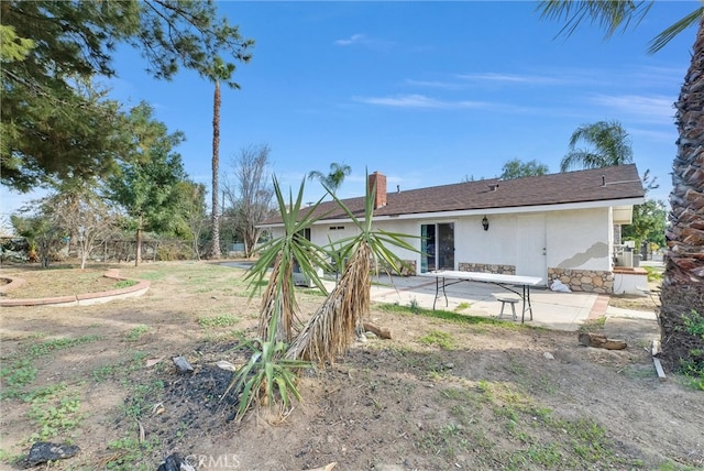 rear view of house featuring stucco siding, stone siding, and a patio