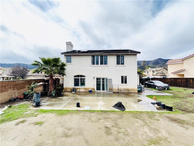 back of house with a patio, a fenced backyard, roof mounted solar panels, and a chimney