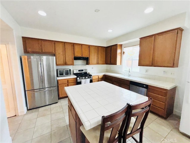 kitchen featuring light tile patterned floors, brown cabinets, appliances with stainless steel finishes, and tile counters