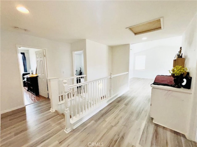 corridor with wood finished floors, attic access, and an upstairs landing