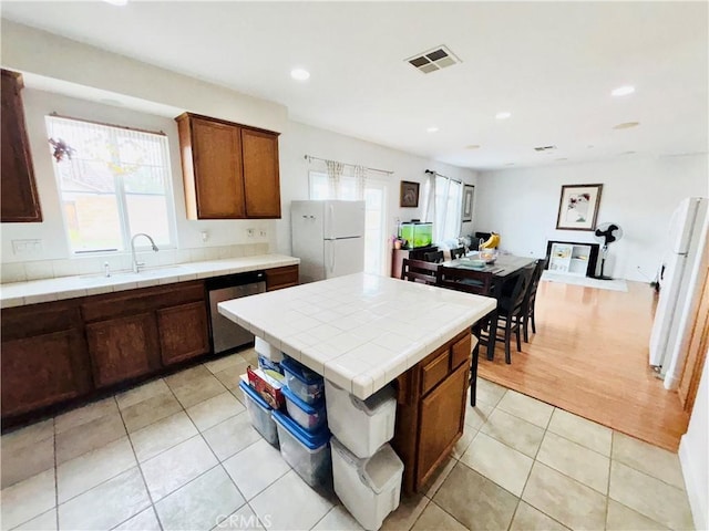 kitchen with tile countertops, visible vents, freestanding refrigerator, a sink, and stainless steel dishwasher