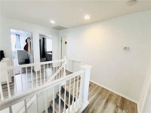 hallway with visible vents, baseboards, light wood-style flooring, recessed lighting, and an upstairs landing