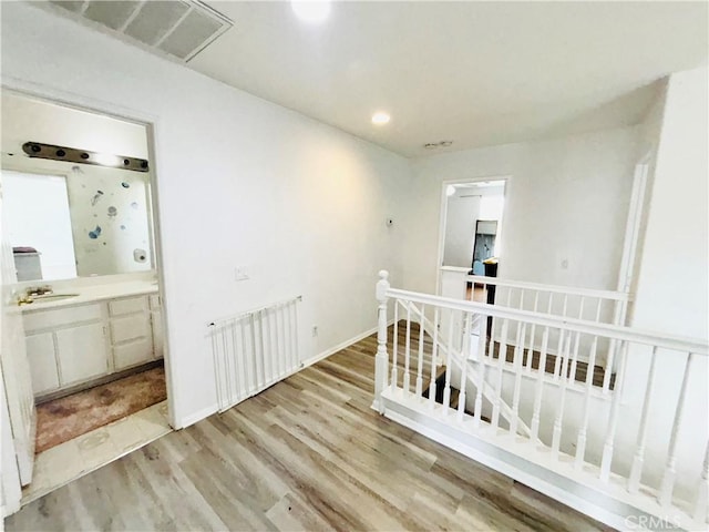 corridor with radiator, visible vents, baseboards, an upstairs landing, and light wood-type flooring