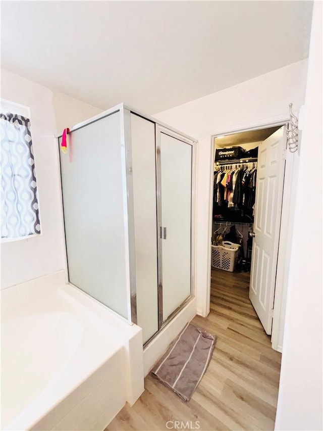 full bathroom featuring a shower stall, a spacious closet, a garden tub, and wood finished floors