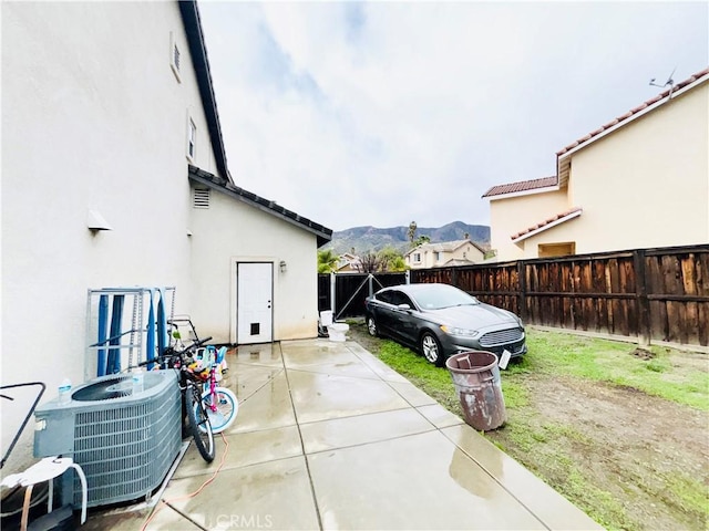 view of side of home with fence, central AC unit, stucco siding, a mountain view, and a patio