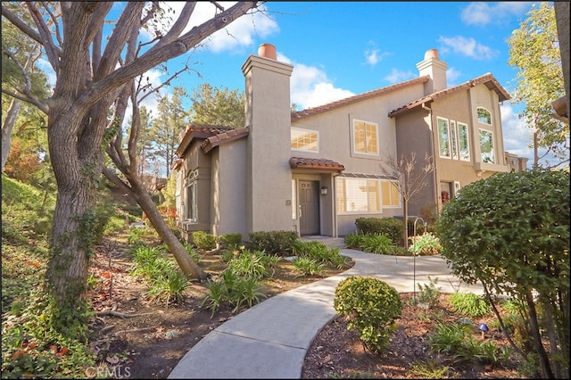 mediterranean / spanish home with stucco siding, a tiled roof, and a chimney