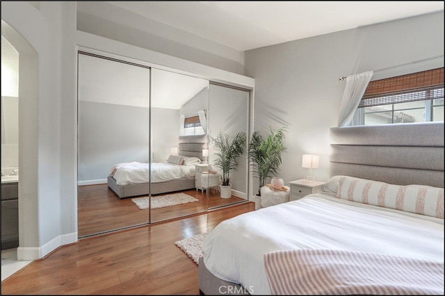 bedroom featuring wood finished floors, a closet, arched walkways, baseboards, and vaulted ceiling