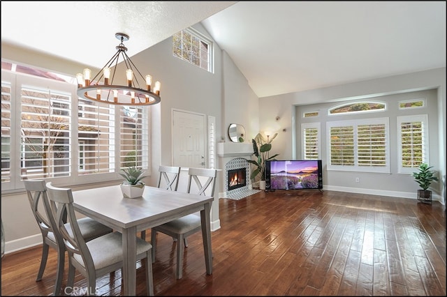 dining space featuring baseboards, a fireplace with flush hearth, a notable chandelier, high vaulted ceiling, and wood-type flooring