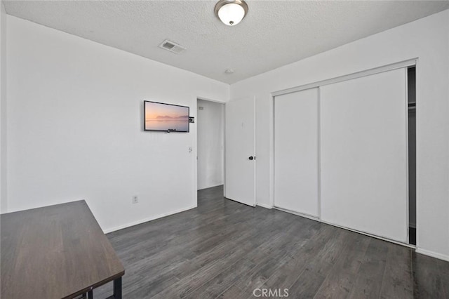 unfurnished bedroom featuring a textured ceiling, a closet, wood finished floors, and visible vents