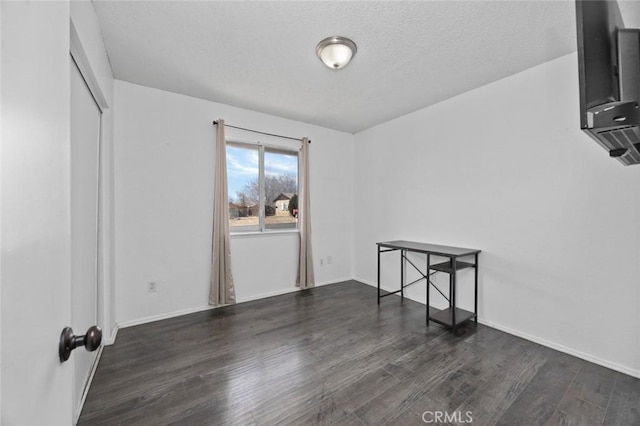 empty room featuring a textured ceiling, wood finished floors, and baseboards