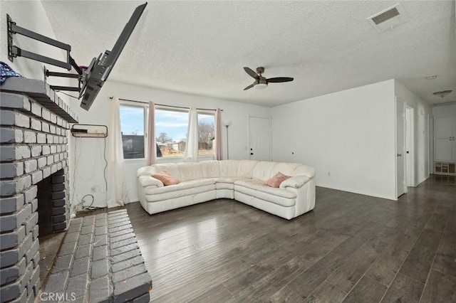 unfurnished living room featuring dark wood finished floors, visible vents, a ceiling fan, a brick fireplace, and a textured ceiling