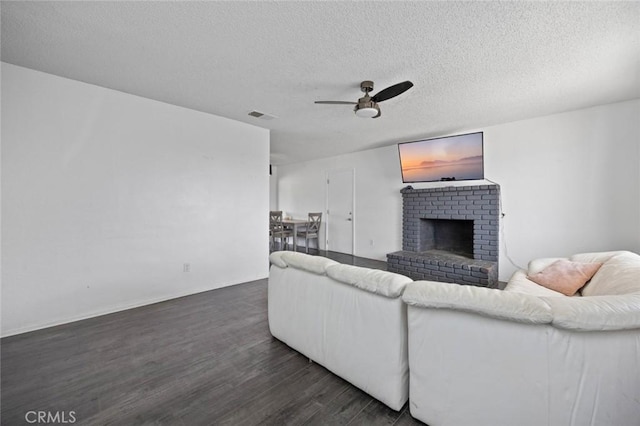 living room with dark wood-style floors, a fireplace, visible vents, ceiling fan, and a textured ceiling