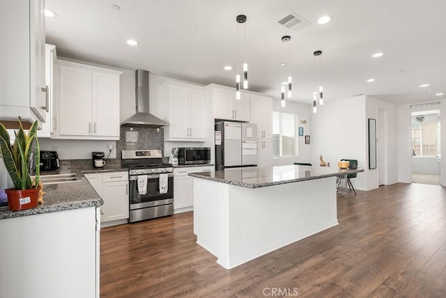 kitchen with stainless steel appliances, dark wood-type flooring, white cabinets, wall chimney range hood, and a center island