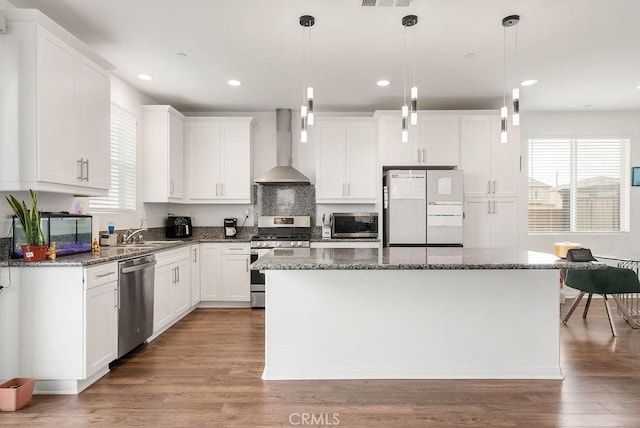 kitchen featuring stainless steel appliances, wood finished floors, a center island, wall chimney exhaust hood, and plenty of natural light