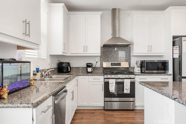 kitchen with wall chimney exhaust hood, appliances with stainless steel finishes, dark wood-type flooring, white cabinetry, and a sink