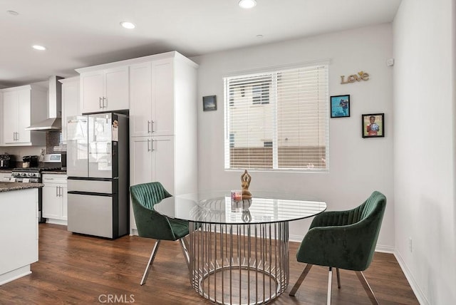 kitchen with dark wood-type flooring, gas stove, freestanding refrigerator, white cabinets, and wall chimney exhaust hood