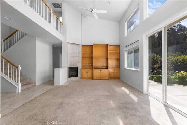 unfurnished living room with visible vents, a tiled fireplace, stairway, light carpet, and a high ceiling