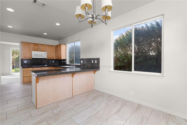 kitchen with visible vents, tasteful backsplash, a peninsula, an inviting chandelier, and white microwave