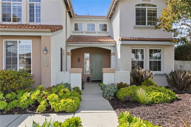 view of exterior entry featuring a tile roof, fence, and stucco siding