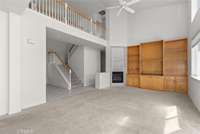 unfurnished living room featuring visible vents, light colored carpet, a towering ceiling, and a fireplace