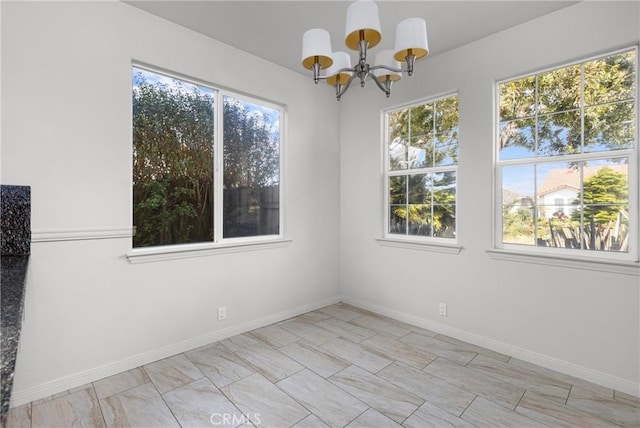 spare room with a wealth of natural light, baseboards, and a chandelier